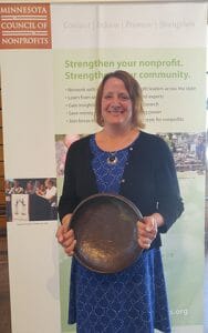 Smiling woman in dress holds bronze bowl in front of Minnesota Council of Nonprofits sign