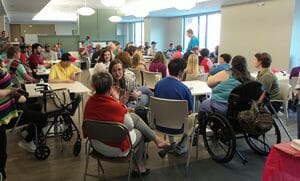 Dozens of people, some in wheelchairs, sit scattered around large room