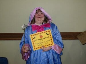Young woman wearing Fairy Godmother costume smiles and holds her certificate for the best female costume for the Ghostly Gala