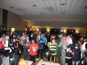 A large diverse group of people in Halloween costumes dancing in dim room