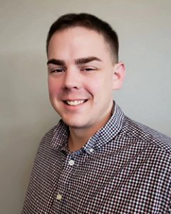 Young man with short, dark hair and wearing a button-up shirt, smiles at the camera