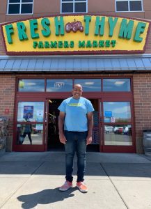 Andrew in a blue shirt standing in front of Fresh Thyme Store.