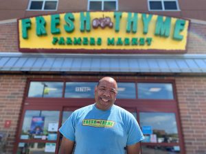 Andrew in a blue shirt standing in front of Fresh Thyme Store.